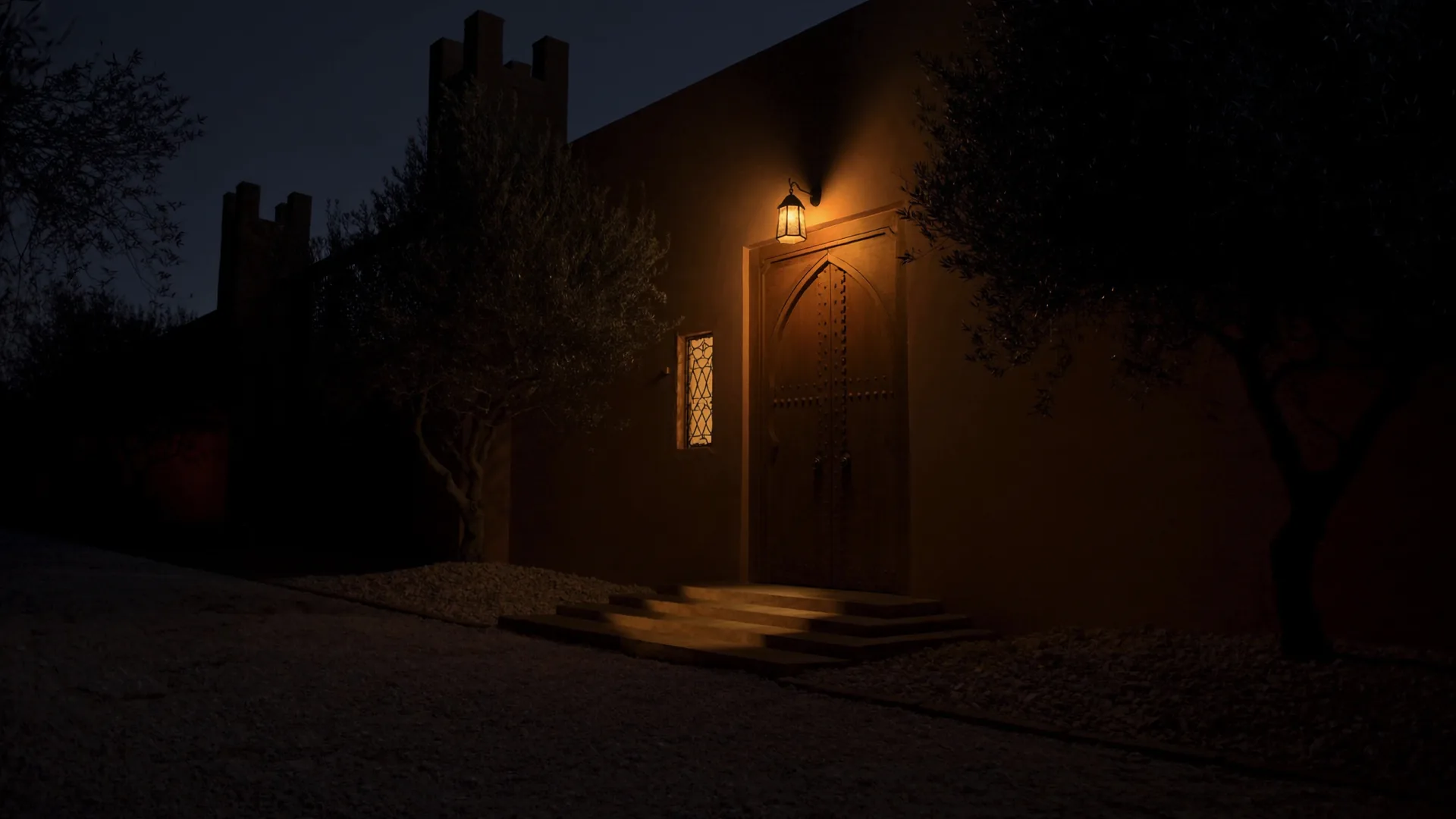La porte d’une villa marrakchie éclairée par une lanterne, la nuit, les marches dans la lumière